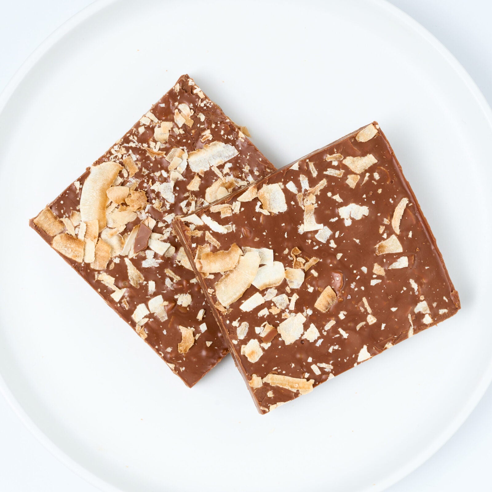 White chocolate almond bark, two thick rectangular pieces studded with whole almonds, stacked on a white round plate.