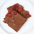 Milk chocolate strawberry bark, large pieces studded with bright red dried strawberry bits, stacked on a white round plate.