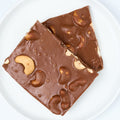 Milk chocolate cashew bark, large square pieces studded with whole roasted cashews, on a white round plate.