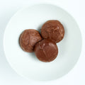 Round milk chocolate covered thin mint patties with smooth shiny coating, plated on white.