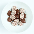 Dark chocolate nonpareils topped with tiny white sprinkles, round candies arranged on a white plate.