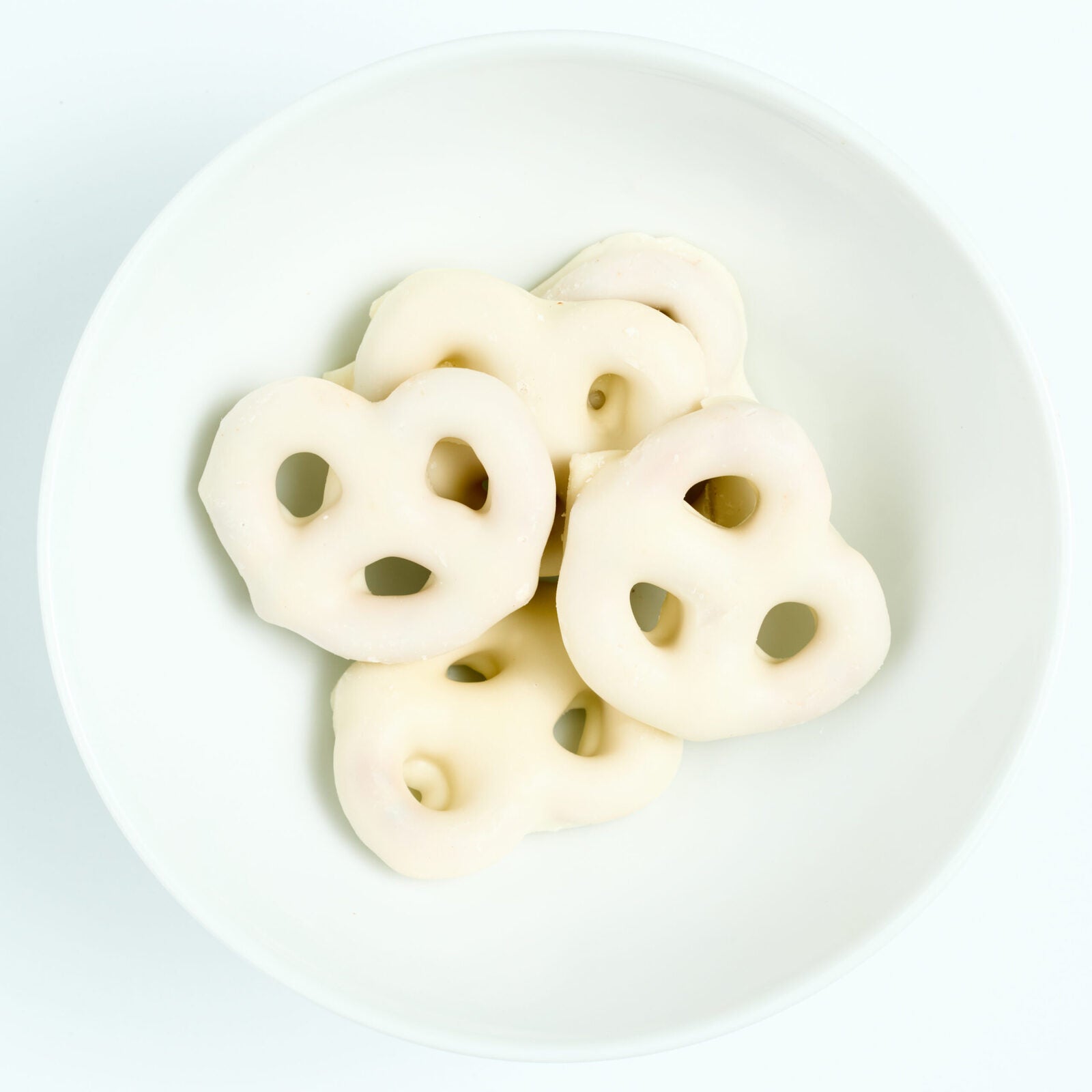Bite-size pretzels fully dipped in smooth white chocolate, plated on white.