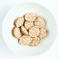 Peanut butter nonpareils topped with tiny white sprinkles, round candies arranged on a white plate.