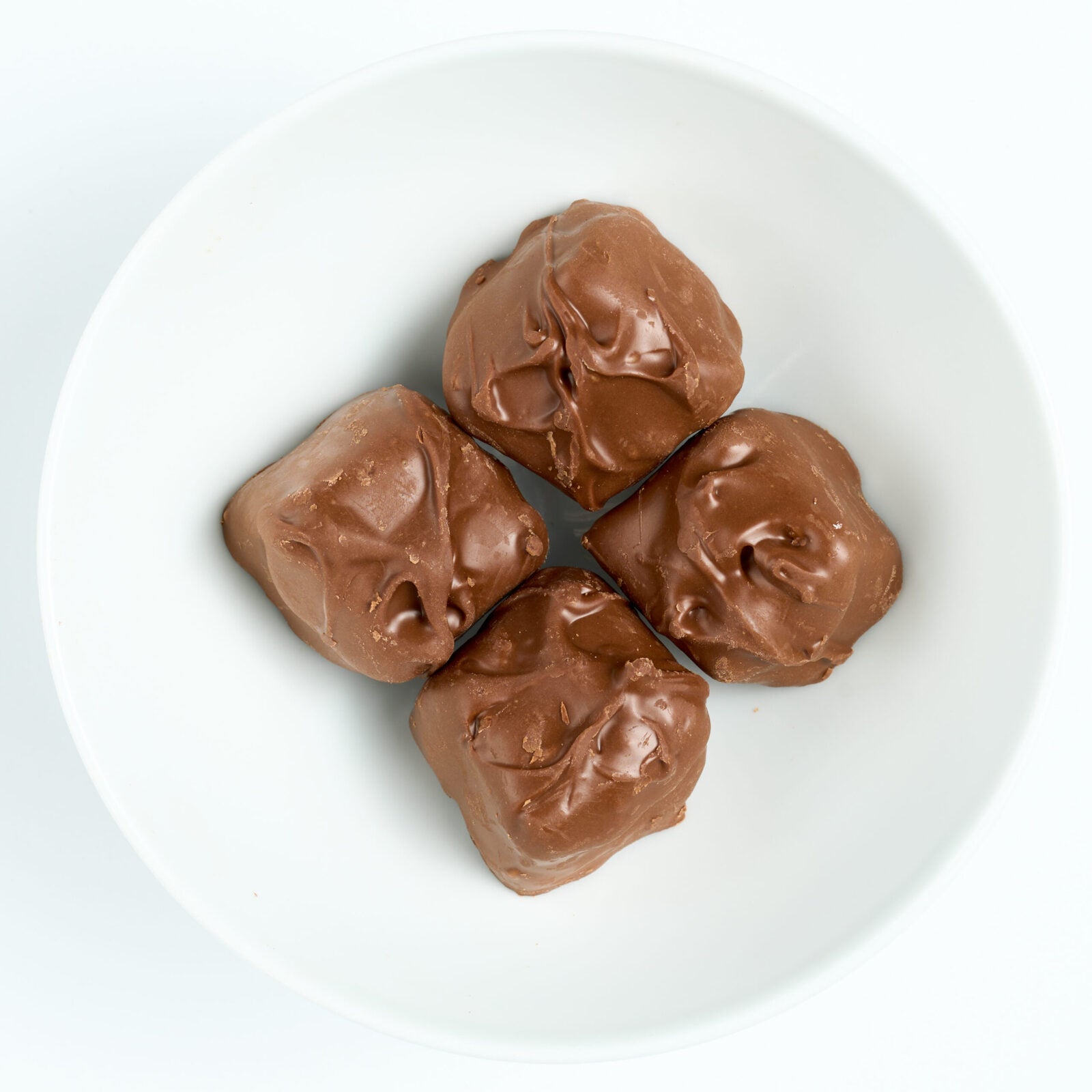 Sugar free milk chocolate covered coconut royal cream pieces with glossy hand-dipped coating, arranged on a white round plate, top view.