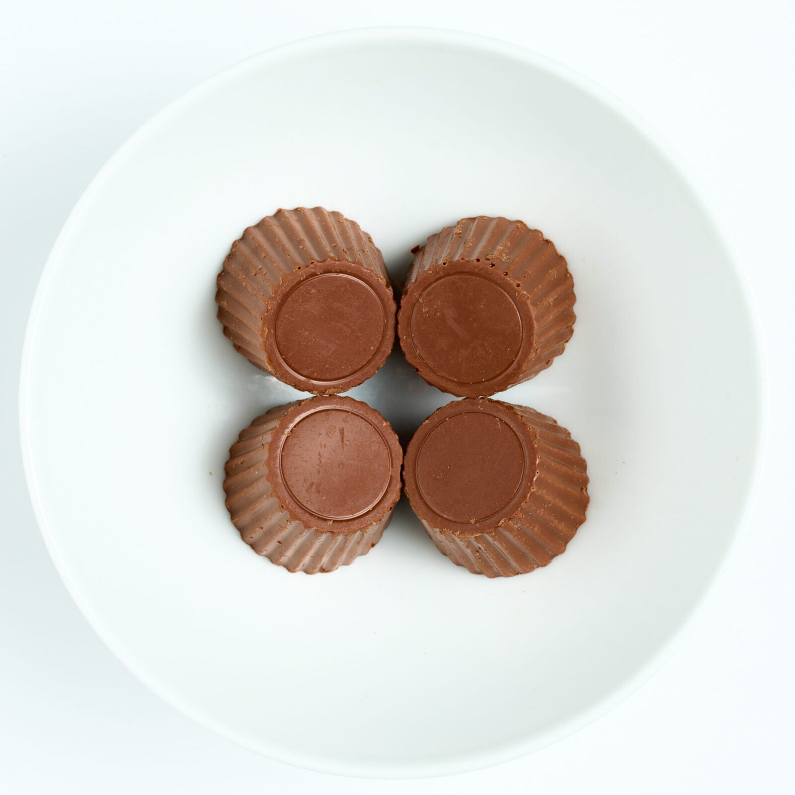 Four sugar free milk chocolate peanut butter cups with fluted edges, arranged on a white round plate, top view.