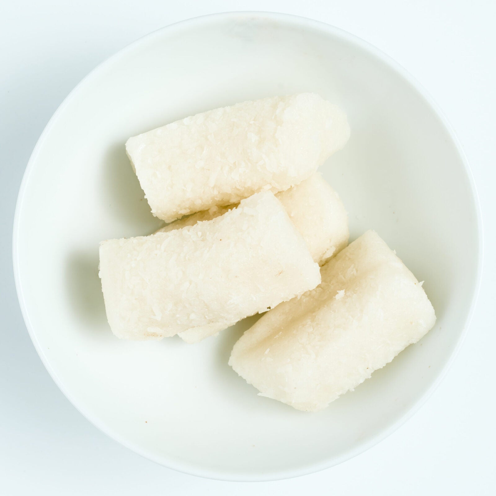 Sugar free coconut snack pieces, soft white shredded-coconut bites, on a white round plate.
