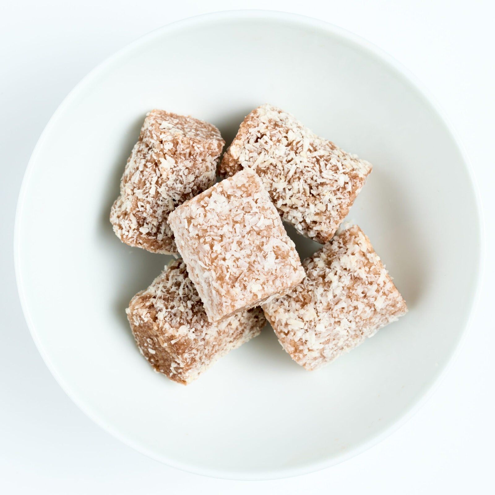 Square cocoa coconut snack bites coated in shredded coconut and cocoa, piled on a white round plate.