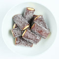Sour cola flavored filled pipe candies, dark brown sugar-coated tubes with pale cream filling visible at the ends, piled on a white plate.