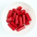 Bite-size red strawberry licorice pieces with ridged edges, piled on a white plate.