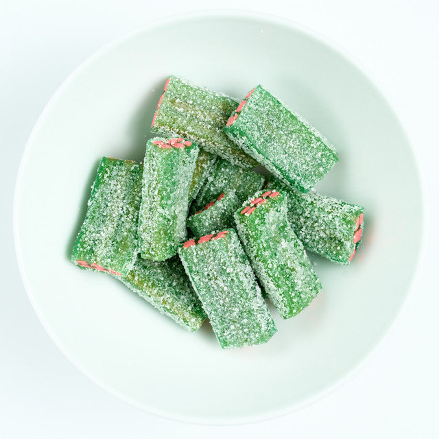 Sour watermelon block licorice pieces with green sugar-coated outside and pink center, piled on a white plate.