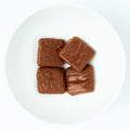 Bite-size graham cracker squares fully coated in smooth milk chocolate, plated on white.