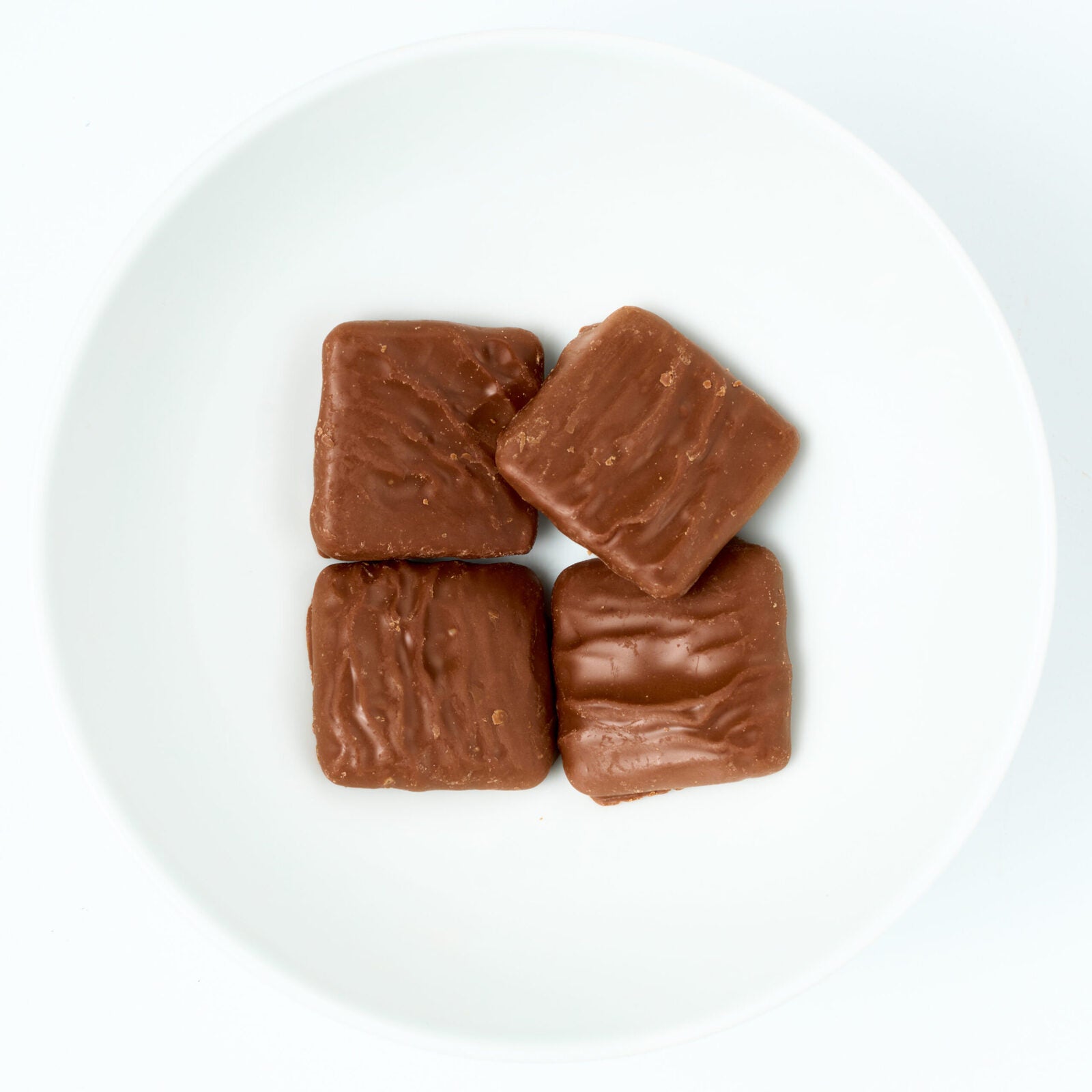 Bite-size graham cracker squares fully coated in smooth milk chocolate, plated on white.